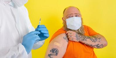 homem com barba e tatuagens faz a vacina contra covid-19 foto