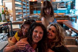 grupo do maduro mulheres estão sorridente e abraçando cada de outros dentro uma bar foto