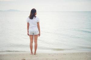 traseiro de uma jovem em pé na praia com os pés descalços foto