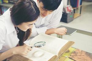 casal de jovens estudantes asiáticos na biblioteca lendo um livro juntos