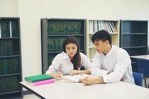 casal de jovens estudantes asiáticos na biblioteca lendo um livro juntos