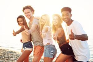 grupo do feliz amigos tendo Diversão às oceano de praia às alvorecer foto