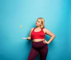 gordo menina tentativas para jogar com mesa tênis. ciano fundo foto