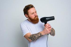 sério homem com barba jogar com cabelo secadoras uma revólver foto