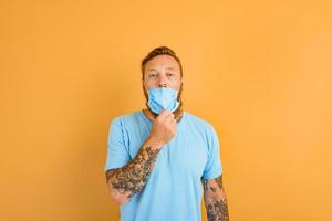 homem com barba e tatuagens quer para retirar a mascarar para covid-19 foto