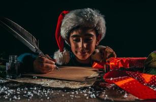 criança com Natal chapéu escreve uma carta para santa claus para presentes foto