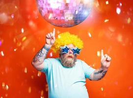 gordo homem com barba, tatuagens e oculos de sol danças música em uma discoteca foto