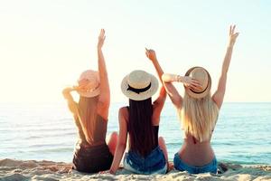 grupo do feliz meninas tendo Diversão às oceano de praia às alvorecer foto