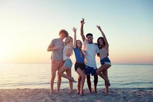 grupo do feliz amigos tendo Diversão às oceano de praia às alvorecer foto