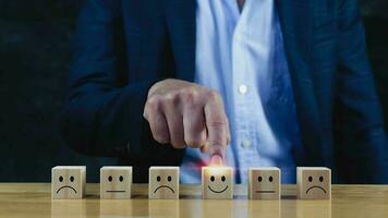 avaliação de serviço ao cliente e pesquisa de satisfação conceitos de classificação de serviço. mão de empresário escolha o bloco de madeira com o ícone de sorriso de rosto feliz no cubo de madeira. foto