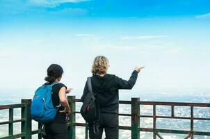 viagem e turismo. a costas Visão do a mulheres mochileiro turista com desfrutando Visão juntos em paisagem urbana a céu e nuvens foto