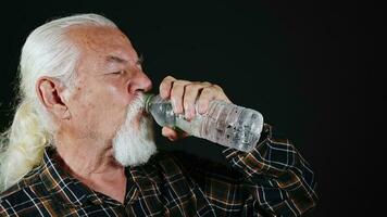 velho branco cabelos homem é bebendo água a partir de plástico garrafa foto