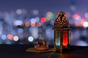 lanterna e pequeno prato de frutas tâmaras com céu noturno e cidade bokeh luz de fundo para a festa muçulmana do mês sagrado do ramadã kareem. foto