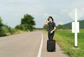 mulher com bagagem pedindo carona ao longo de uma estrada foto