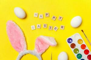 inscrição feliz Páscoa cartas ovos colorida tintas e Coelho orelhas isolado em na moda amarelo fundo foto