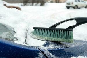 a de capuz do uma carro é limpo com uma escova depois de uma queda de neve foto