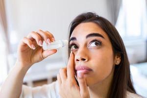 visão e oftalmologia remédio. fechar-se do lindo mulher aplicando colírio dentro dela olhos. jovem fêmea modelo com natural Maquiagem usando uma garrafa do olho gotas. saúde conceito. Alto resolução foto