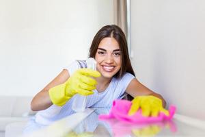 lindo jovem mulher faz limpeza a casa. menina esfrega pó. sorridente mulher vestindo borracha protetora amarelo luvas limpeza com trapo e spray garrafa detergente. lar, serviço de limpeza conceito. foto