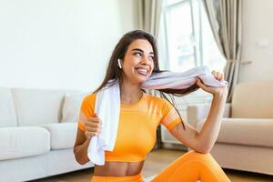 lindo jovem mulher limpando suor com uma toalha, Exausta depois de a diariamente treinamento.atraente jovem mulher levando uma pausa enquanto exercício às lar. foto