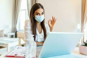 quarentena, controlo remoto trabalho e pandemia conceito - mulher vestindo face protetora médico mascarar para proteção a partir de vírus doença com computador portátil computador mostrando Está bem placa foto