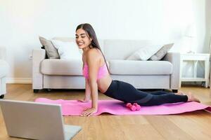 menina Treinamento às lar, fazendo exercite-se e assistindo videos em computador portátil, Treinamento dentro vivo sala. lindo mulher é fazendo lado prancha exercício. ela é assistindo vídeo em a Internet e recorrente a tarefas foto