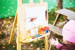 pequeno menina desenha em a cavalete. a criança tintas foto