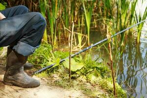 uma homem senta em a rio banco e pega peixe. homem é pescaria em a lago costa foto