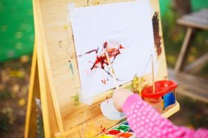 pequeno menina desenha em a cavalete. a criança tintas foto