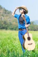 mulher usa chapéu e carrega seu violão no campo de grama foto