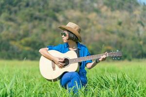 mulheres de cabelo curto usam chapéu e óculos de sol sentam-se tocando violão no campo de grama foto