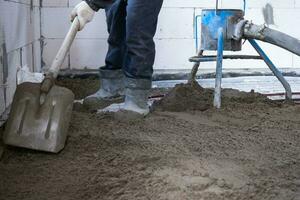 semi seco chão mesa - uma trabalhador pás uma construção mistura através uma especial manga para cimentação e nivelamento em debaixo do chão aquecimento tubos. foto