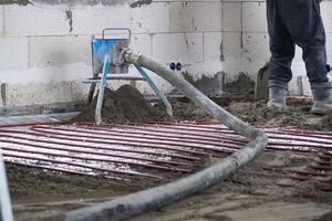 semi seco chão mesa - uma trabalhador pás uma construção mistura através uma especial manga para cimentação e nivelamento em debaixo do chão aquecimento tubos. foto