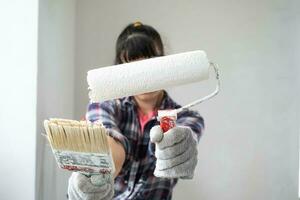 intrigado mulher dentro pintura rolo e branco pintura para paredes dentro mãos fechar-se retrato. construção trabalhos e Cosmético reparos dentro casa, parede pintura, tingimento, acabamento trabalhos com seu próprio mãos foto