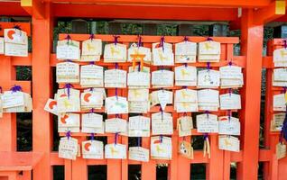 Quioto, Japão, 2018 desejando de madeira tag com bênção texto a partir de pessoas e turista em vermelho de madeira pólo às Fushimi Inari santuário. foto