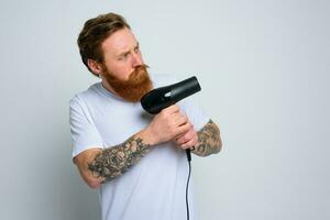 sério homem com barba jogar com cabelo secadoras uma revólver foto
