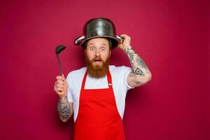 espantado chefe de cozinha com barba e vermelho avental tocam com Panela foto