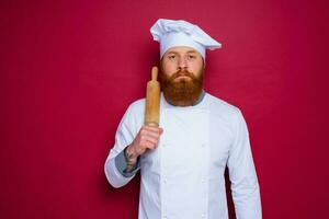 sério chefe de cozinha com barba e vermelho avental chefe de cozinha detém de madeira rolando PIN foto