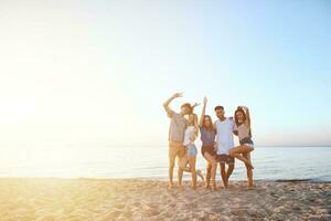 grupo do feliz amigos tendo Diversão às oceano de praia às alvorecer foto
