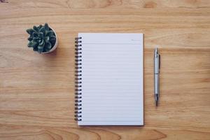 em branco caderno e lápis em madeira mesa com Panela plantar. foto