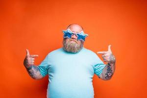 gordo duvidoso homem com barba, tatuagens e oculos de sol é incerto para alguma coisa foto