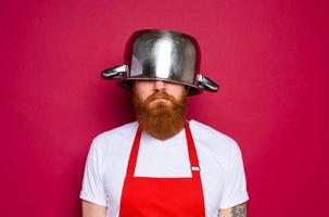 infeliz chefe de cozinha com barba e vermelho avental tocam com Panela foto