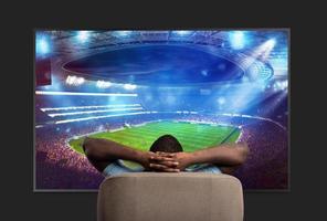 espectador dentro frente do uma ampla televisão relaxado em a poltrona às casa assistindo uma Esportes jogos foto