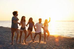 grupo do feliz amigos tendo Diversão às oceano de praia às alvorecer foto