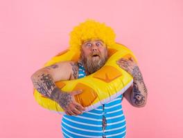 gordo espantado homem com peruca dentro cabeça é pronto para nadar com uma rosquinha salva-vidas foto
