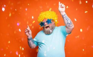 gordo homem com barba, tatuagens e oculos de sol danças música em uma discoteca foto