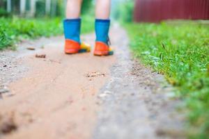 criança dentro borracha chuteiras caminhando ar livre. criança pés dentro uma borracha bota foto