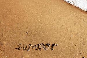 palavra verão escrito a mão em a arenoso de praia com onda e cópia de espaço foto