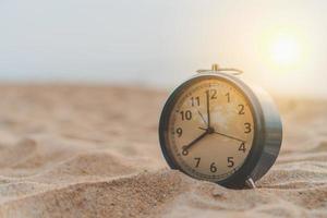 close-up de um relógio na areia com fundo de luz do sol foto