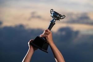 um homem segurando uma taça de troféu contra o fundo do céu nublado do crepúsculo foto