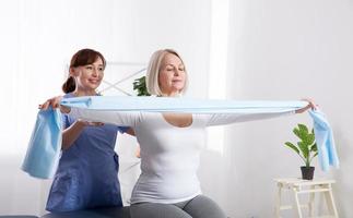 fisioterapeuta e mulher sentada em uma cama se exercitando com uma fita de borracha foto